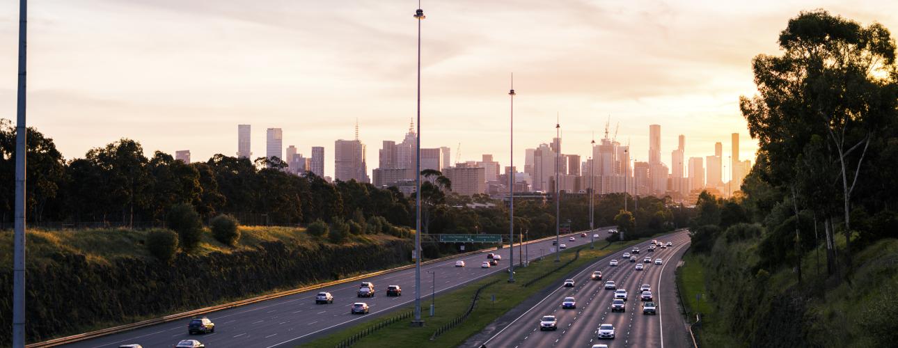 Cars travelling on a freeway with a city skyline in the background of the image